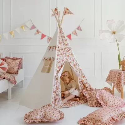 Tenda infantil floral rosa com almofadas e menina sentada dentro num quarto branco