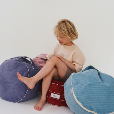 Criança sentada em pufe azul claro com outros pufes coloridos em fundo branco