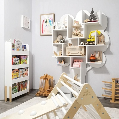 Quarto infantil com prateleira em forma de árvore e estante com livros e brinquedos de madeira.