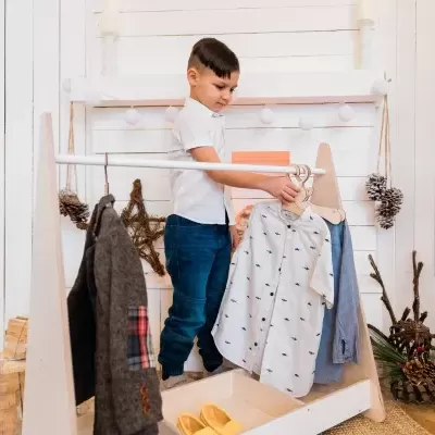 Criança a escolher roupa em cabide com parede e chão de madeira