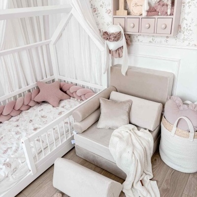 Quarto de bebé com cama branca, almofada estrela rosa, sofá bege, manta branca, cestinho palha e prateleira decorativa