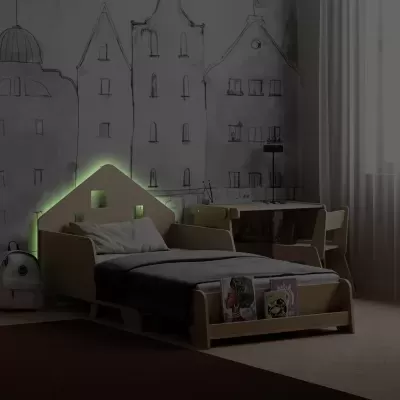Cama infantil de madeira clara com cabeceira em forma de casa iluminada em verde numa divisão com secretária e parede com desenho de edifícios.