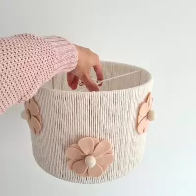 Luminária pendente branca com flores cor de rosa claro em tecido, segurada por mão vestindo camisola rosa