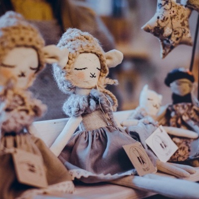 Bonecas de tecido vestidas com roupas em tons neutros sentadas numa prateleira de madeira