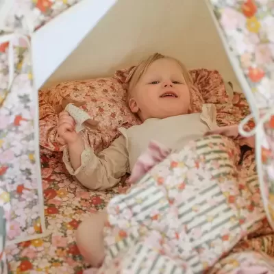 Criança deitada em tenda com padrão floral e mantas coloridas