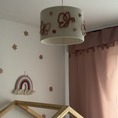 Candeeiro de tecto branco com borboletas cor de rosa e decoração de parede com cortinas rosa.