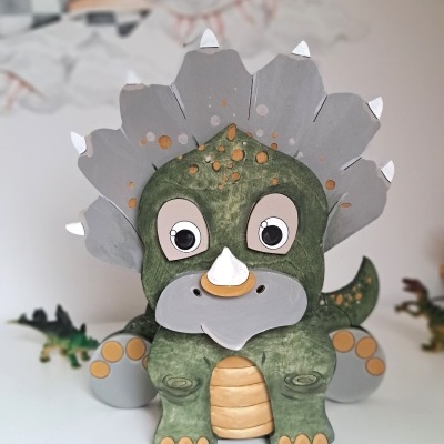 Figura decorativa de dinossauro verde e cinzento com chifres brancos.