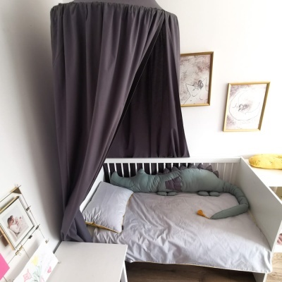 Cama de bebé branca com dossel cinzento, almofadas e decoração ambiental