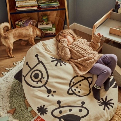 Saco de feijão bege com desenhos espaciais a preto numa sala infantil e criança deitada em cima