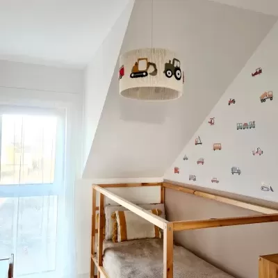 Quarto infantil com cama de madeira em forma de casinha e candeeiro com desenhos de veículos.