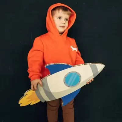 Criança com camisola laranja e brinquedo de foguetão de cartão