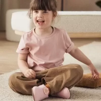 Criança com roupa rosa e castanha sentada em tapete interior