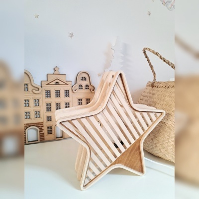 Escultura em madeira em forma de estrela com ripas horizontais e fundo com miniaturas de edifícios e cesto de palha.