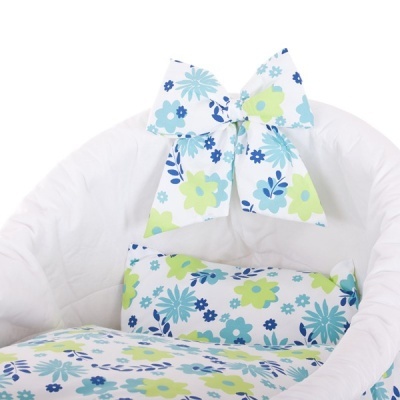 Berço acolchoado branco com almofadas e laço decorativo floral azul, verde e branco