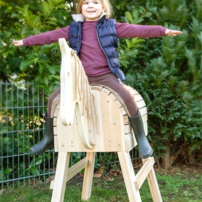 Criança sentada num cavalo de balanço de madeira num jardim