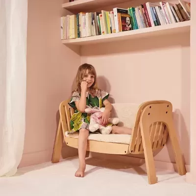 Criança num sofá infantil de madeira segurando ursinho de peluche