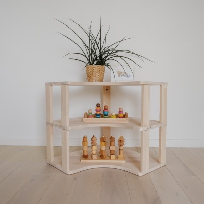 Estante de madeira clara com três níveis, planta, figuras de madeira coloridas e peças de xadrez