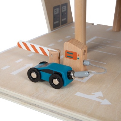 Brinquedo de carro em madeira azul com cancela laranja e branca sobre base de madeira pintada com sinais de trânsito