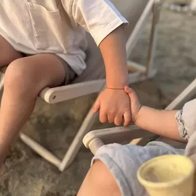 Crianças sentadas em cadeiras de praia com areia, segurando as mãos e um cone de gelado.