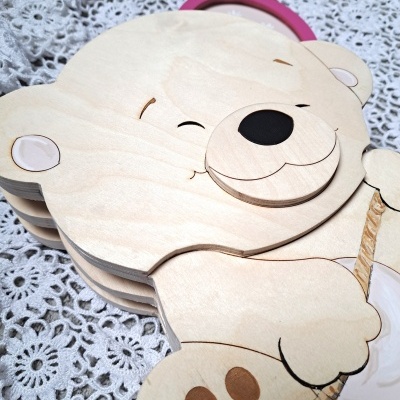 Livro de madeira em forma de urso alegre com nariz preto sobre toalha rendada branca