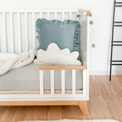 Berço branco com colchão cinza, almofadas azul e branca e manta felpuda