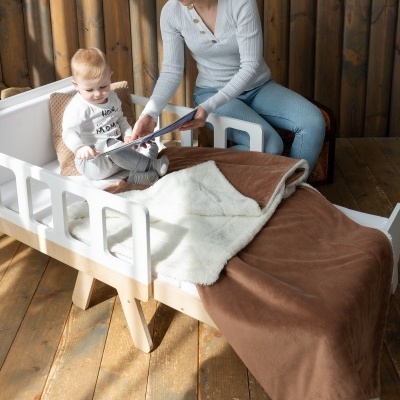 Cama infantil branca de madeira com cobertores e criança sentada