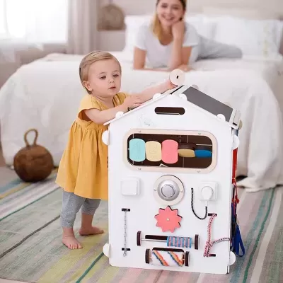 Brinquedo educativo em forma de casinha branca com atividades sensoriais coloridas e criança a brincar.