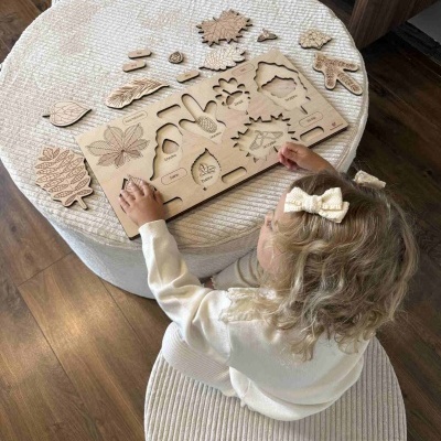 Criança brincando com quebra-cabeças de madeira com formas de folhas e pinhas