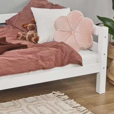 Cama branca com roupa de cama castanha e almofadas, incluindo almofada em forma de flor cor-de-rosa