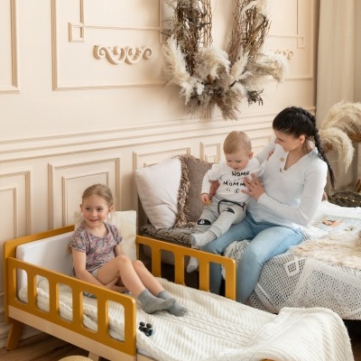 Quarto infantil com cama amarela, cama maior, mulher e bebé, guirlanda decorativa na parede