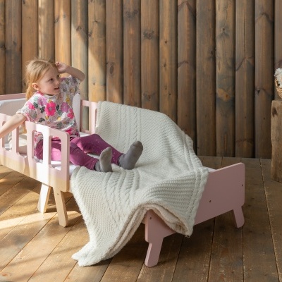 Cama infantil rosa com manta de tricô creme em ambiente rústico de madeira