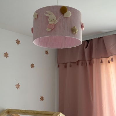 Candeeiro rosa de teto com decoração de coelho em quarto com paredes brancas e cortinas rosa