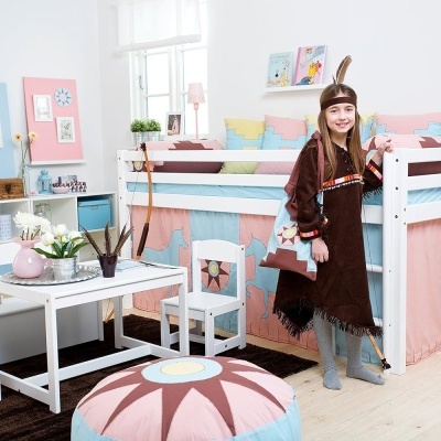 Quarto infantil decorado com cama alta, mesa branca, almofadão colorido e menina fantasiada