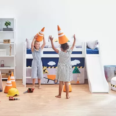 Quarto infantil moderno com cama tipo beliche branca com escorrega e têxtil azul decorativo, crianças a brincar com cones de trânsito de brinquedo.