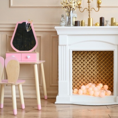 Conjunto de mesa de madeira rosa com espelho geométrico e cadeiras infantis ao lado de lareira decorativa branca