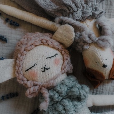 Dois bonecos de pano com roupas de malha em tons suaves sobre fundo de tecido cinza