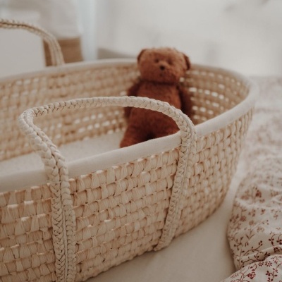 Cesto de bebé tecido com urso de peluche castanho numa cama com colcha branca floral