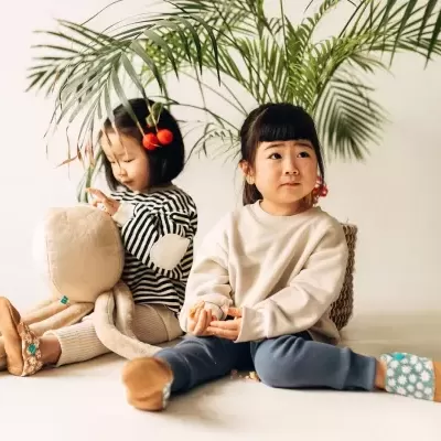 Duas crianças sentadas no chão com roupas confortáveis e um polvo de peluche grande junto a elas, plantas verdes ao fundo.