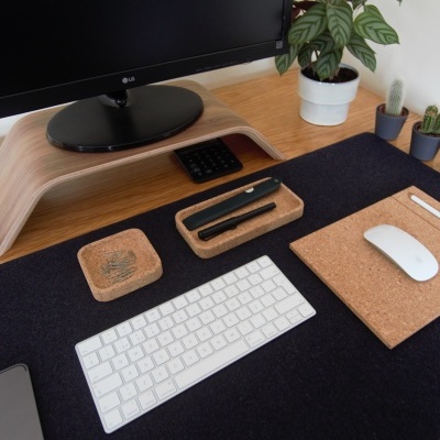 Secretária com tapete preto, teclado branco, rato em placa de cortiça e plantas em vasos pequenos