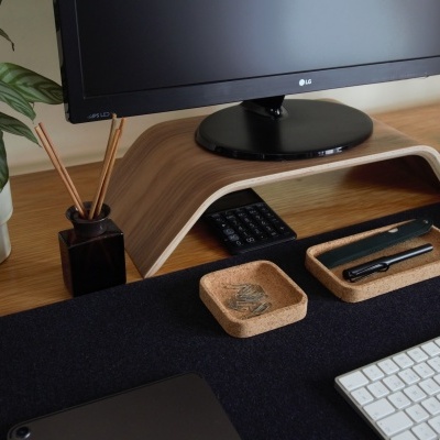 Suporte de monitor em madeira clara com itens de escritório numa secretária