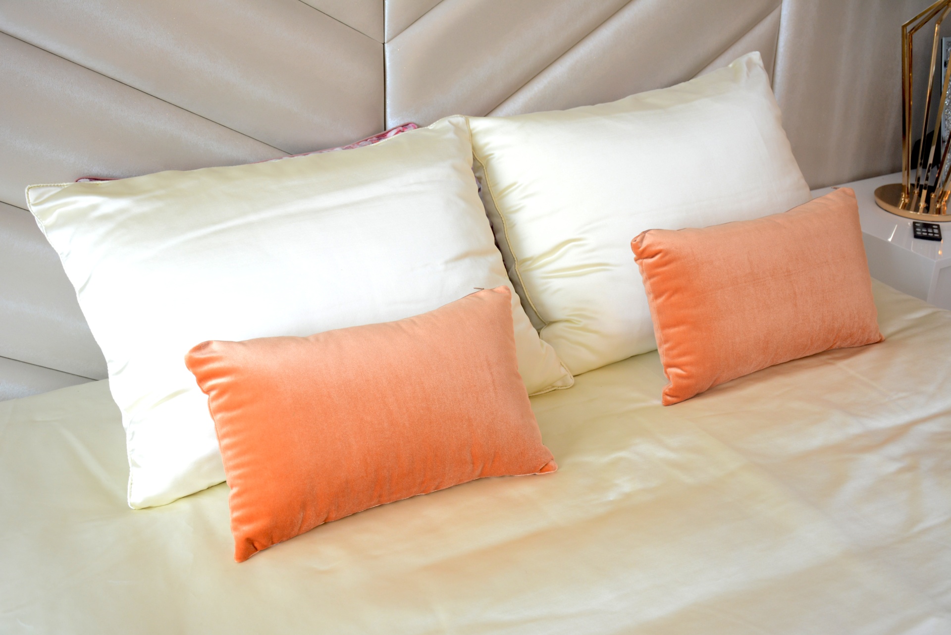 Almofadas brancas e laranjas em cama com cabeceira acolchoada