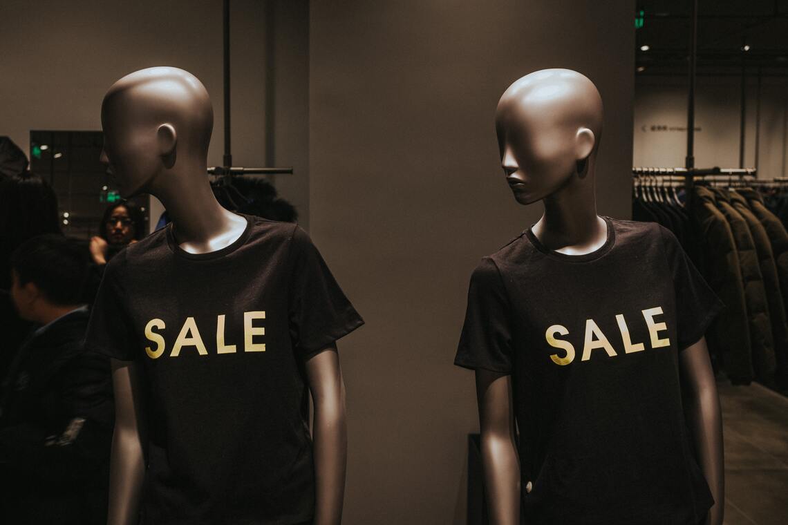 Dois manequins com t-shirts pretas e palavra SALE impressa à frente numa loja de roupa.