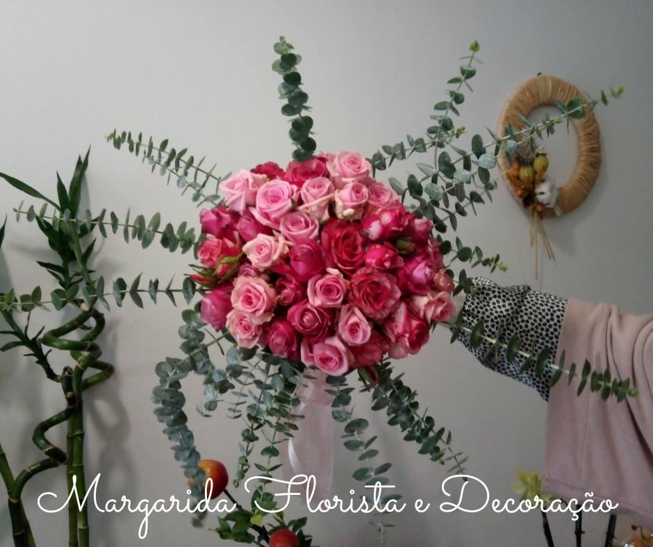 Bouquet grande de rosas rosa com folhagem verde prateada sendo segurado por uma mão