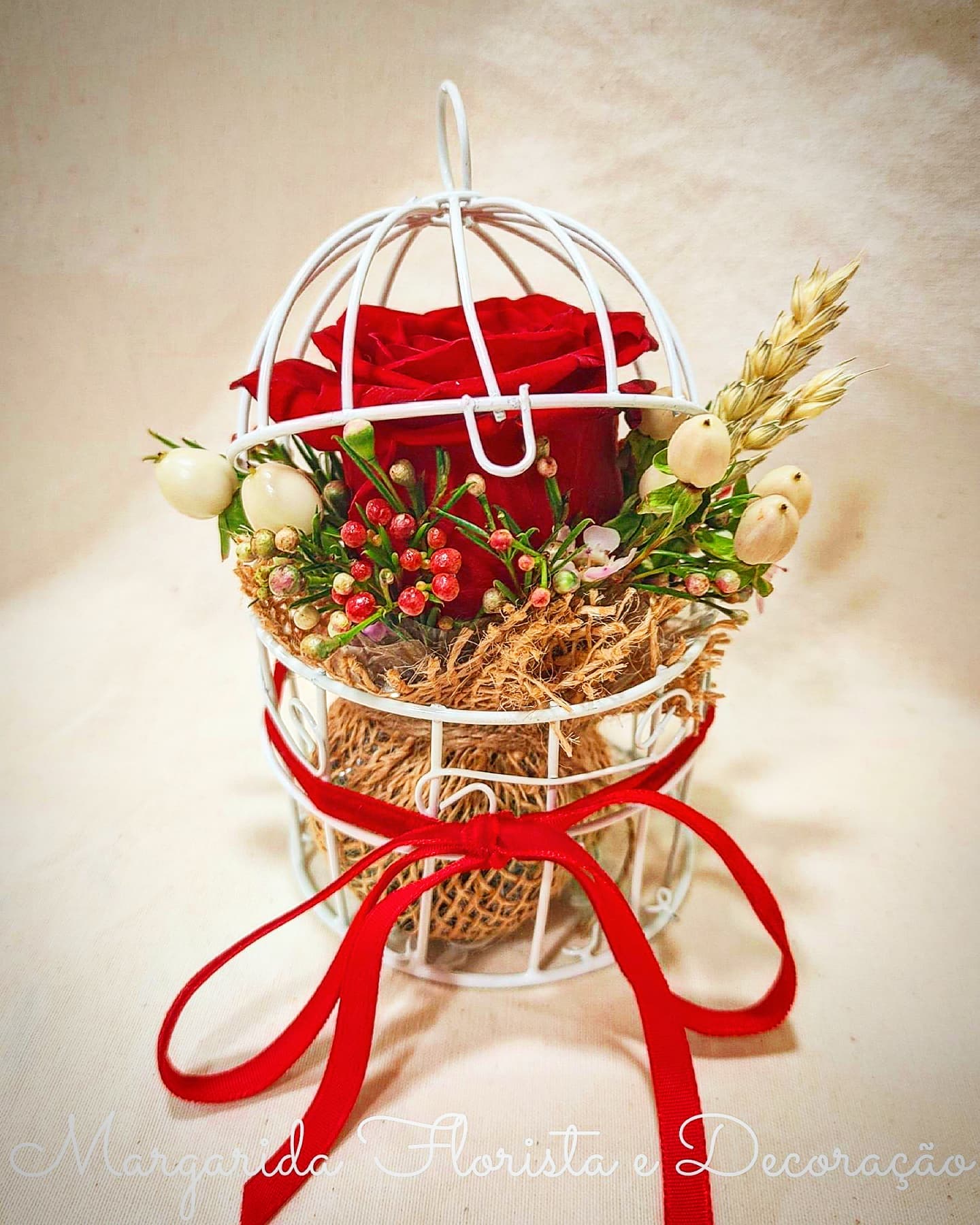 Arranjo floral com rosa vermelha dentro de gaiola branca e fita vermelha