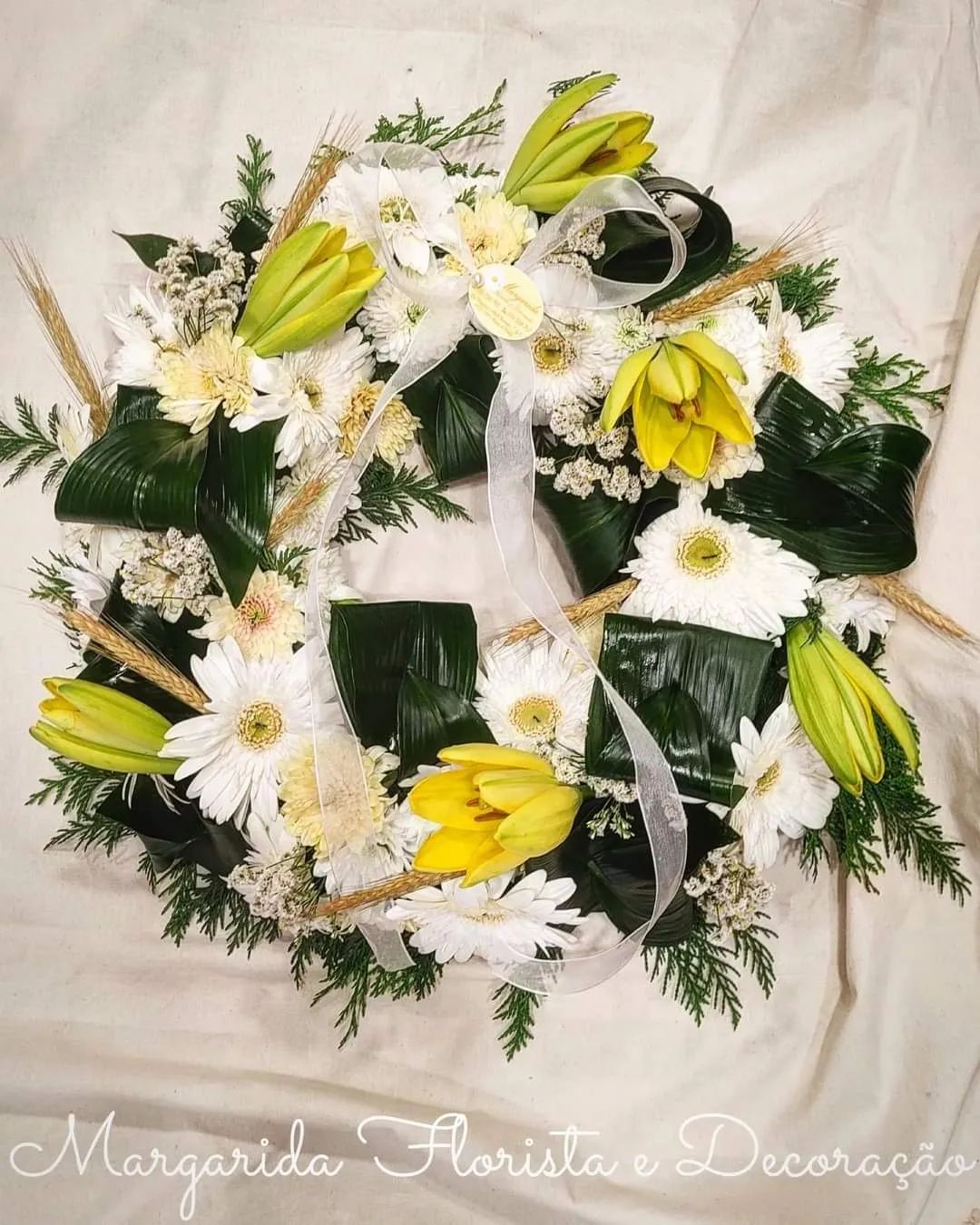 Ramo circular de flores amarelas e brancas com folhagem verde e fita branca sobre fundo branco