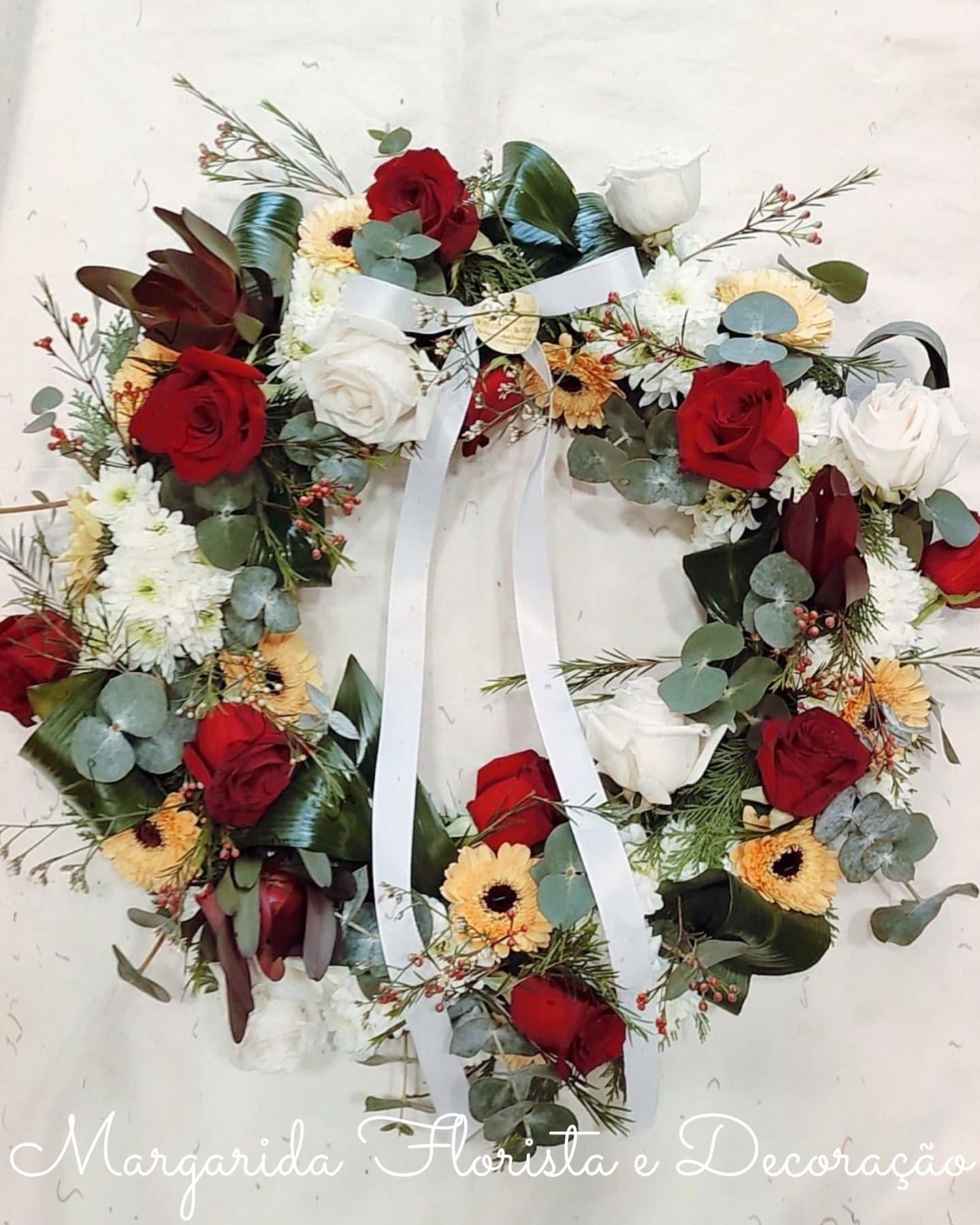 Guirlanda floral em forma de coração com rosas vermelhas e brancas e fitas brancas