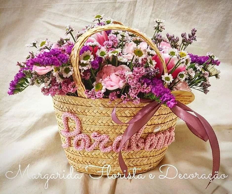 Cesto de palha com flores naturais rosa e lilás e palavra Parabéns bordada