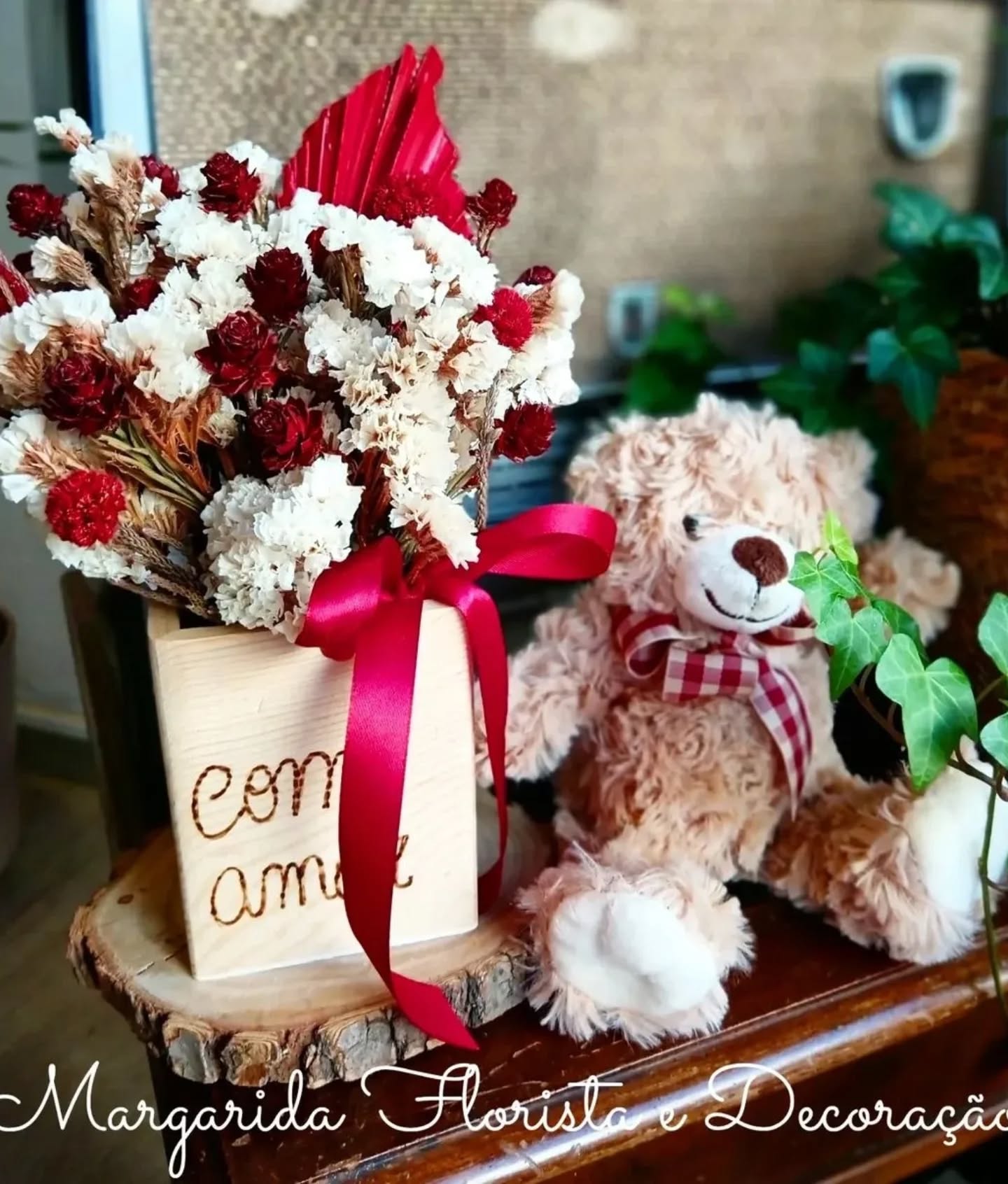 Arranjo de flores secas vermelhas e brancas com urso de pelúcia castanho claro num ambiente decorativo