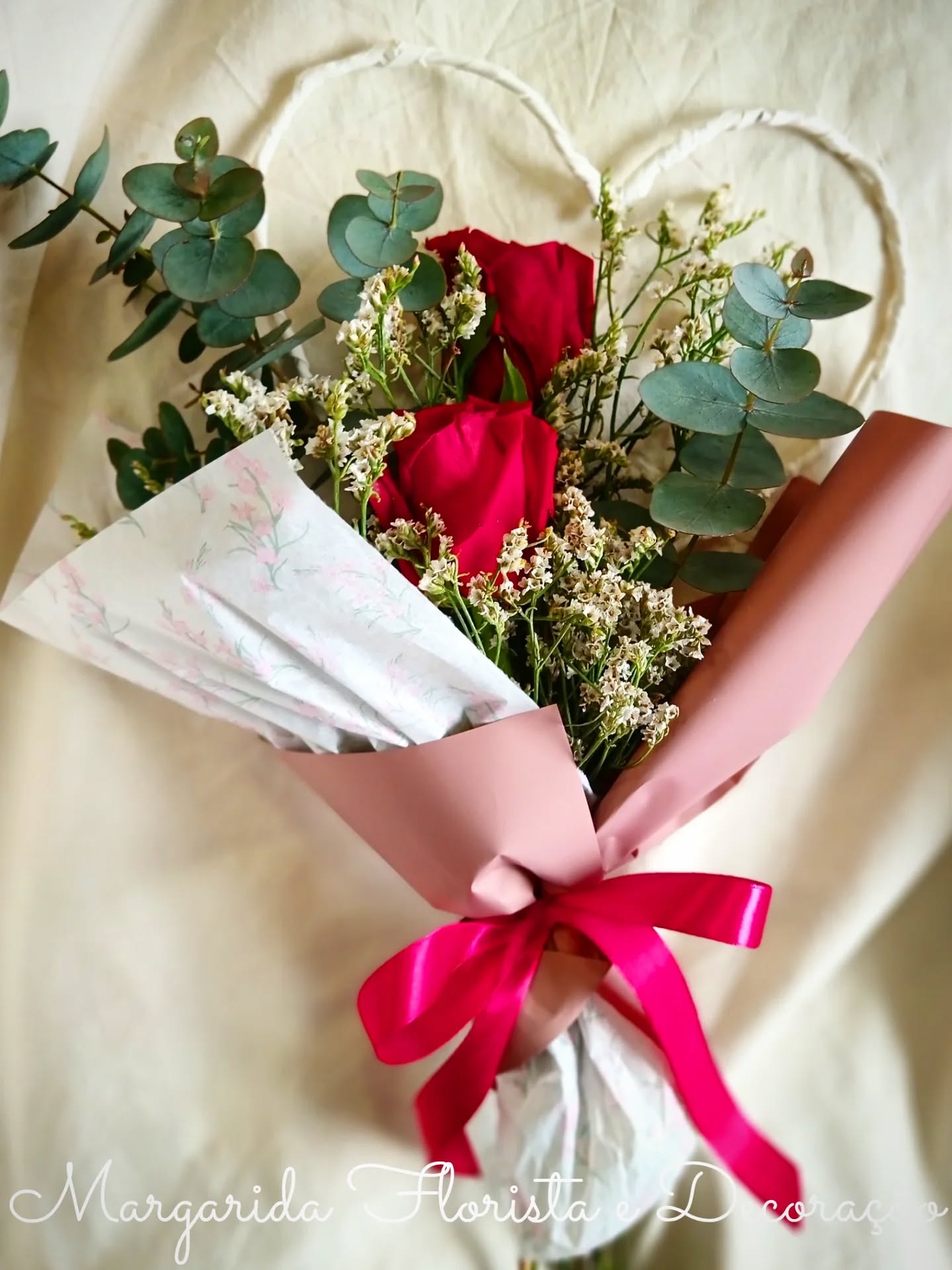 Buquê de rosas vermelhas e folhagem embrulhado com papel rosa e branco com laço rosa
