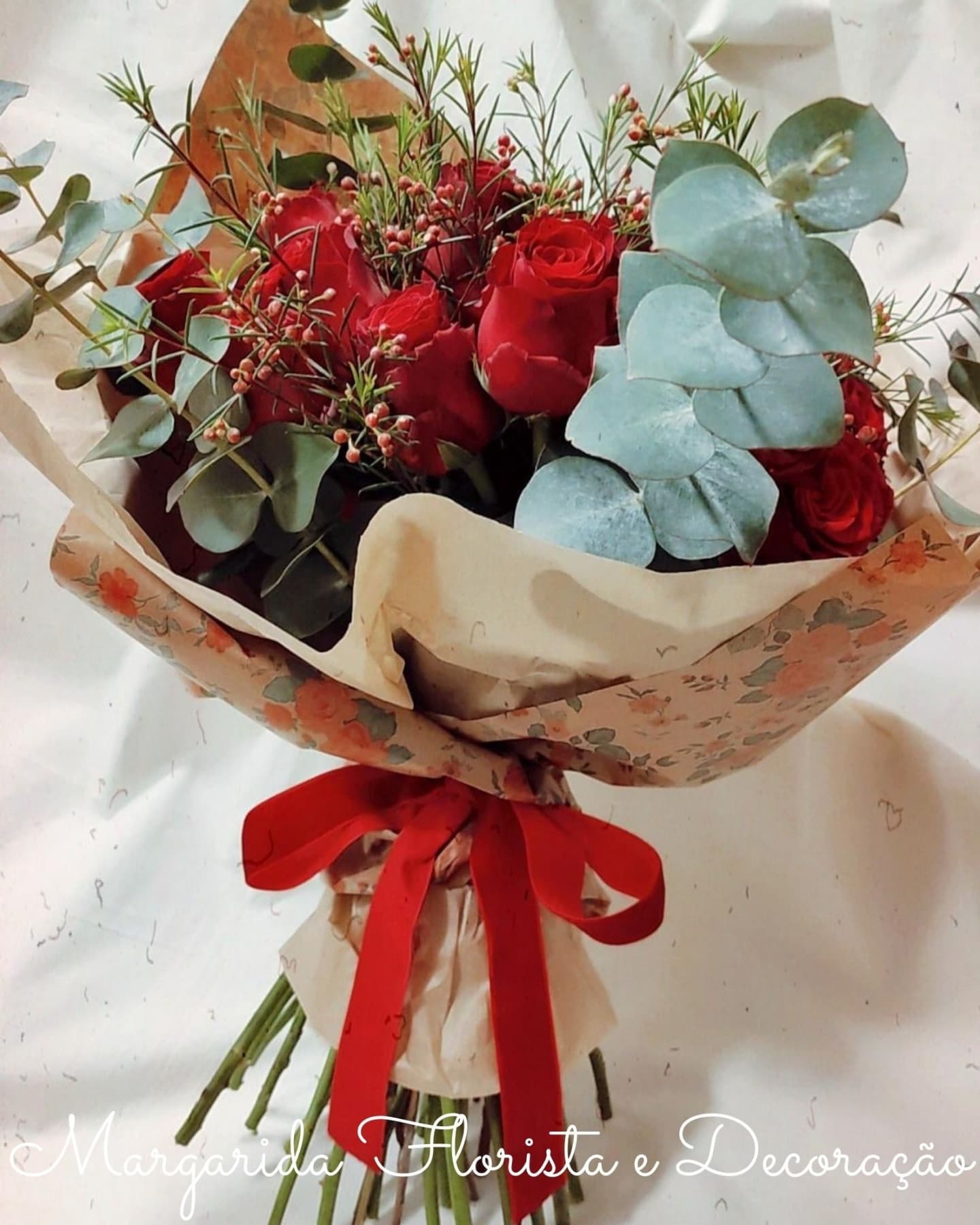 Buquê de flores rosas vermelhas e eucalipto em papel floral com fita vermelha